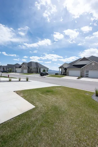 Street view showcasing a row of single-story residences featuring stone and siding exteriors, attached garages, and concrete driveways