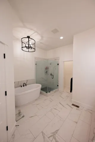 Spacious bathroom featuring large format marble-look tile flooring, a freestanding soaking tub with matte black fixtures, a corner glass-enclosed shower, and an overhead drum pendant light fixture