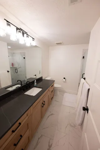 Double vanity featuring a black countertop with integrated sinks, wood-finish cabinetry, and matte black hardware