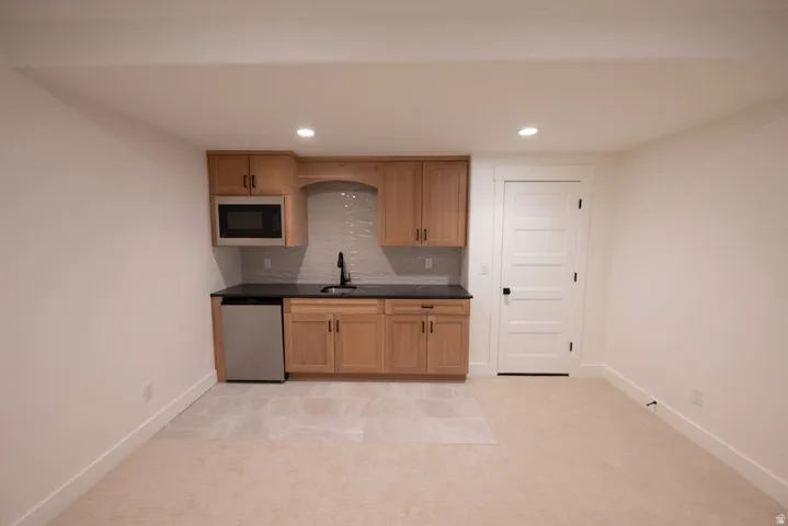 Kitchenette featuring light wood cabinetry, black countertop, stainless steel microwave, and compact refrigerator