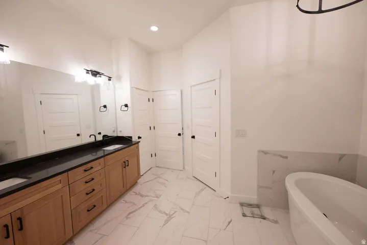 Bathroom featuring a dual vanity with wood cabinetry and black countertops, white vessel sinks, and a freestanding bathtub