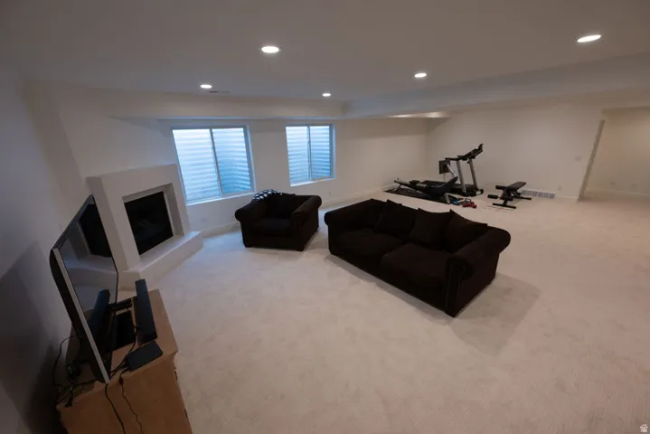 Spacious finished room featuring light-colored carpeting, a fireplace with a white surround, and recessed lighting