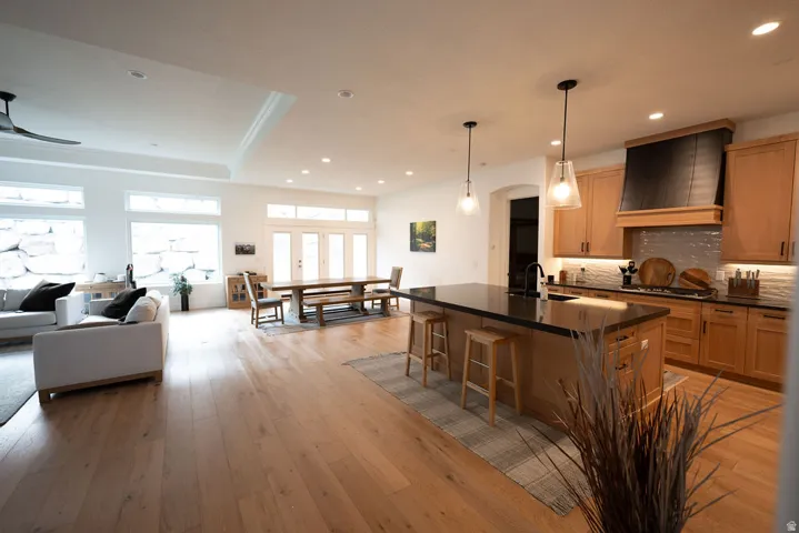 Open-concept interior featuring wood-finish flooring, a kitchen island with seating, pendant lighting, and a kitchen with light-tone cabinetry and a dark range hood
