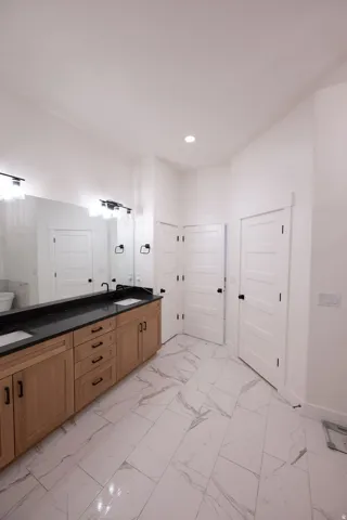 Bathroom featuring a dual vanity with light wood cabinetry and black countertops