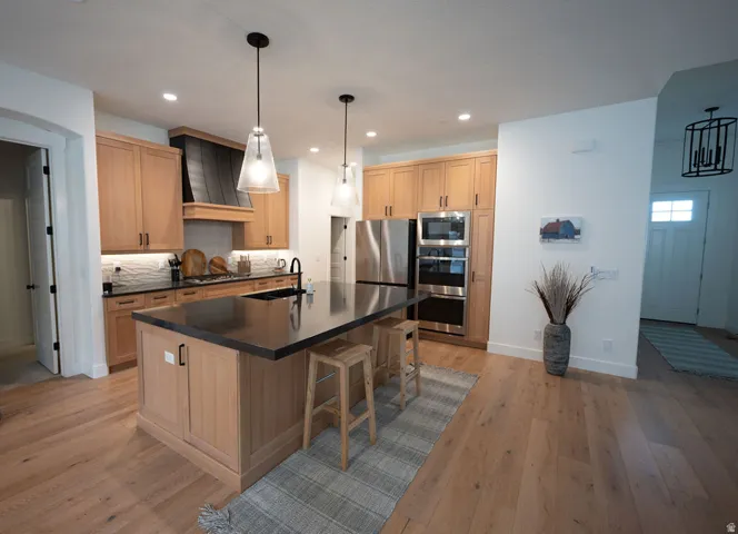 Contemporary kitchen featuring light wood cabinetry, a dark countertop island, stainless steel appliances, and wood-finish flooring