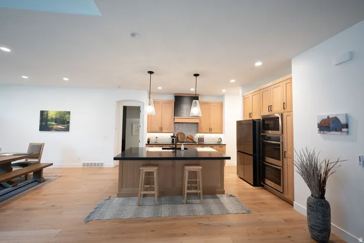 Kitchen featuring light wood-finish cabinetry, a central island with a dark countertop, integrated appliances, and recessed lighting