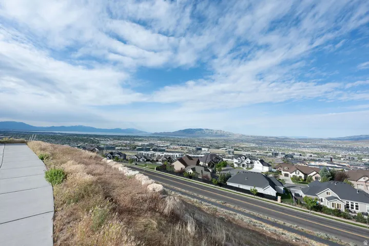 Expansive elevated property featuring a paved sidewalk, natural landscaping, a street below, and distant mountain ranges with a body of water