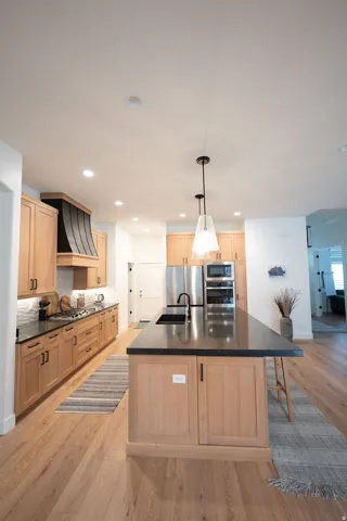 Kitchen featuring light wood cabinetry, dark countertops, wood-finish flooring, recessed lighting, and stainless steel appliances