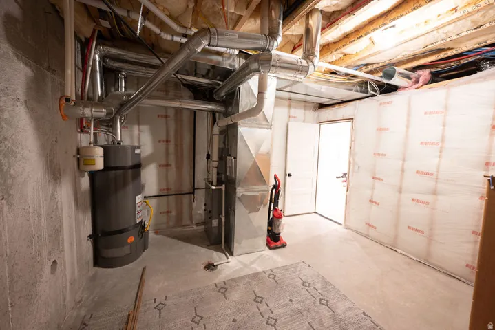Unfinished basement space featuring a concrete floor, exposed ceiling joists, and a water heater installation