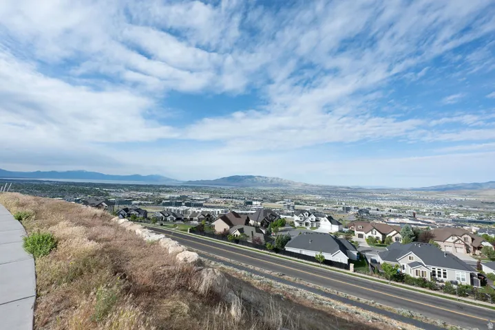 Expansive elevated panorama featuring distant mountains and a body of water, with a residential area visible below
