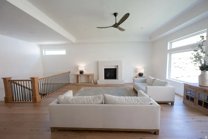 Spacious living area featuring wood-finish flooring, a contemporary fireplace with a light-toned surround, and a ceiling fan