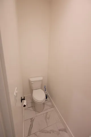 Powder room featuring a white toilet, white walls, black toilet paper holder, and large format white and gray patterned tile flooring