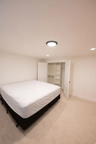 Bedroom featuring neutral-toned carpeting, white walls, and a built-in closet with shelving
