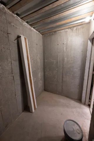 Concrete walled room with exposed ceiling joists and unfinished concrete flooring