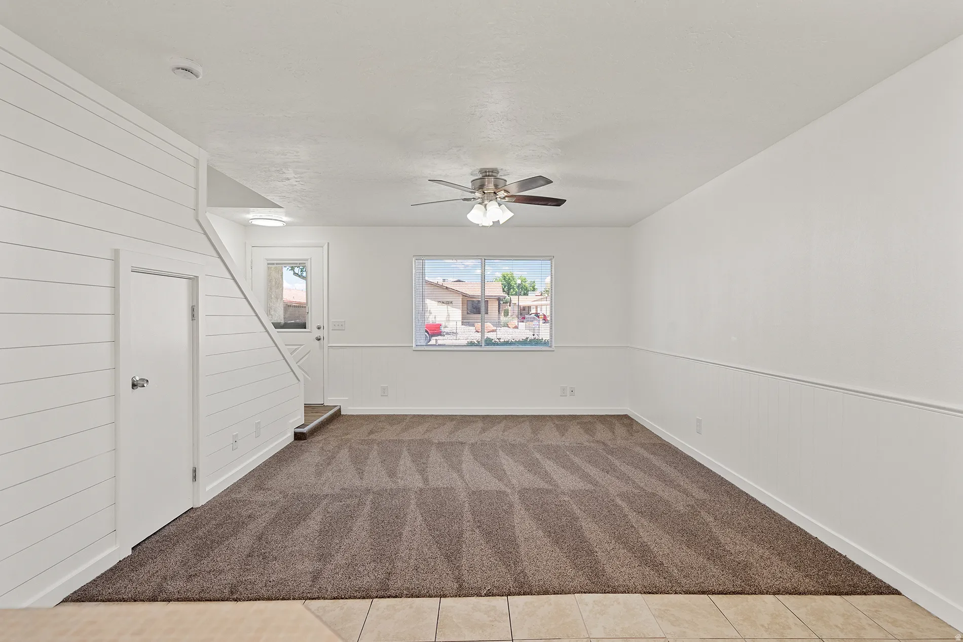 Spacious room featuring shiplap wall accents, a ceiling fan with integrated lighting, and a patterned carpet
