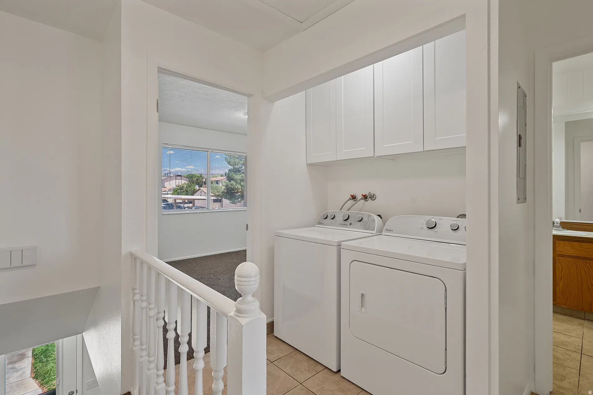 Dedicated laundry area featuring white shaker-style cabinetry, tile flooring, and a balustrade railing