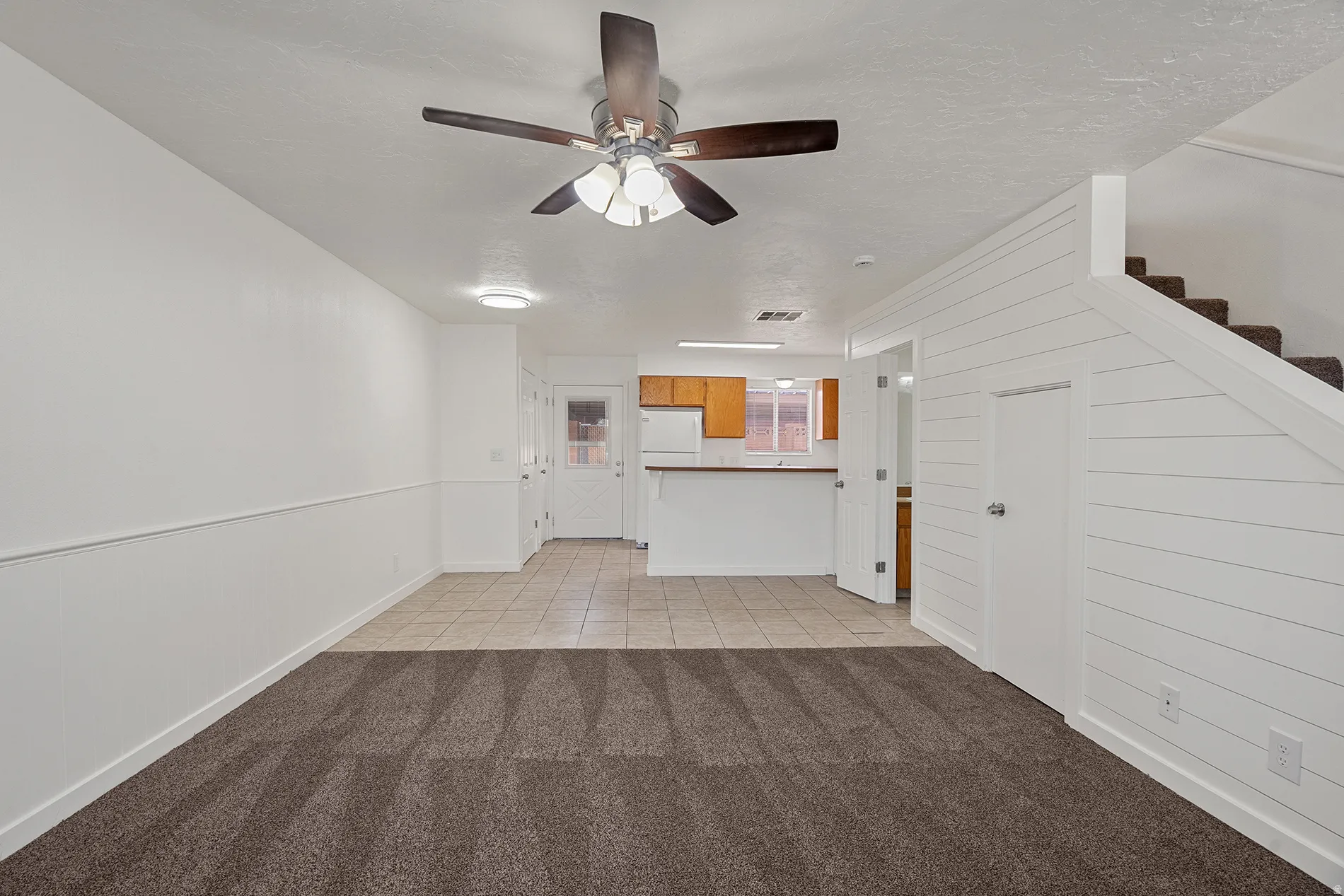 Open-concept living area featuring a ceiling fan with integrated lighting, shiplap accent wall, and wood-finish staircase