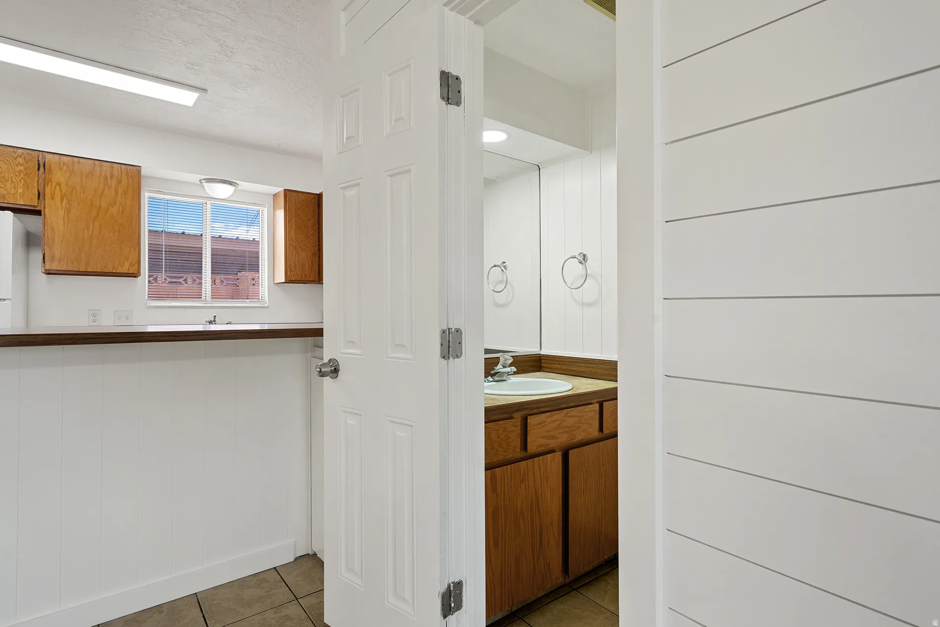 Kitchen and bathroom spaces featuring wood cabinetry, a window over the sink, and tile flooring