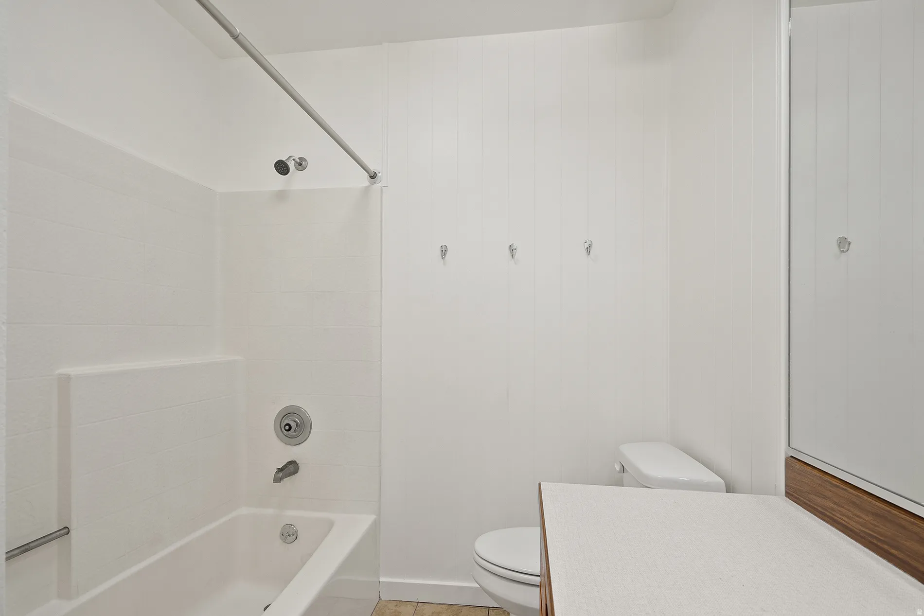 Bathroom featuring a white tub/shower combination with a textured surround, a white toilet, and a vanity with a white countertop and wood-finish base