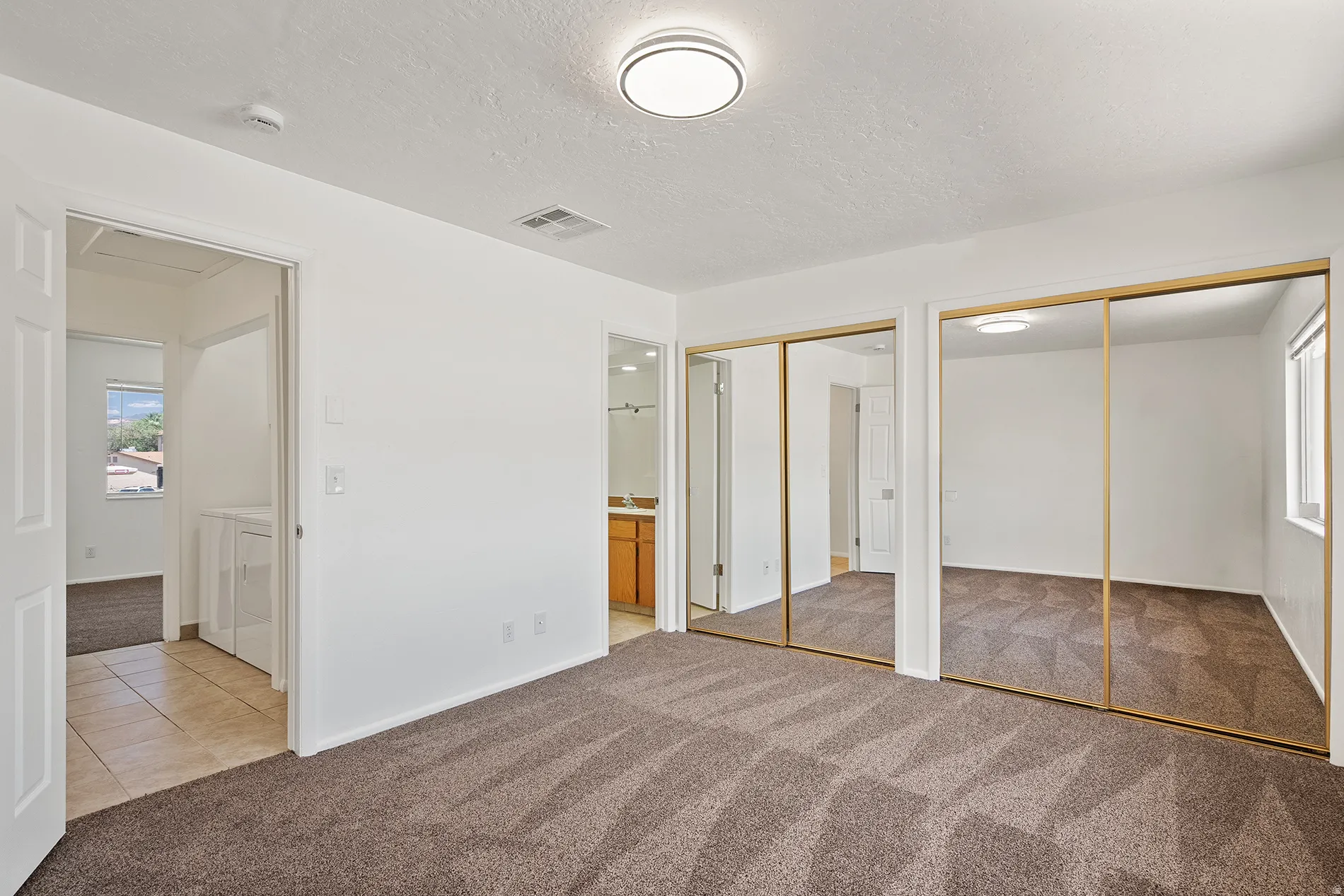 Carpeted bedroom with a neutral color palette, mirrored closet doors, and an overhead flush-mount light fixture