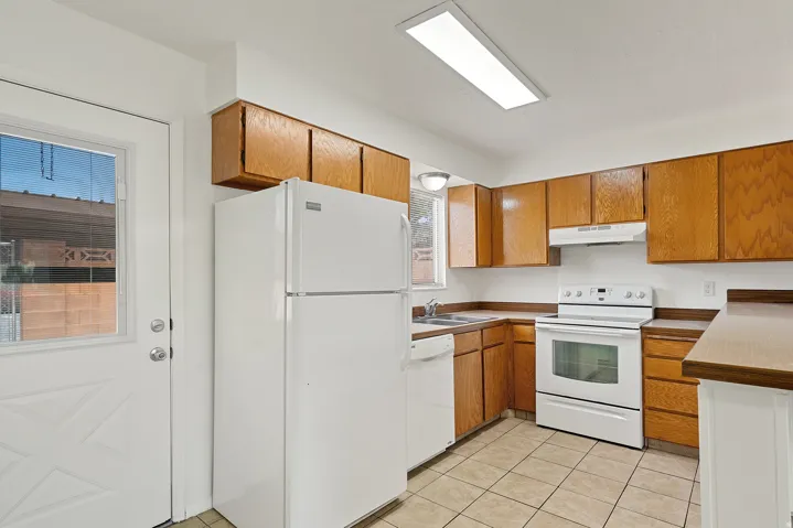Kitchen featuring wood cabinetry, laminate countertops, a white appliance suite, tile flooring, and a glass-paned exterior door