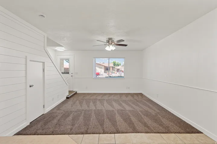 Spacious room featuring shiplap wall accents, a ceiling fan with integrated lighting, and a patterned carpet