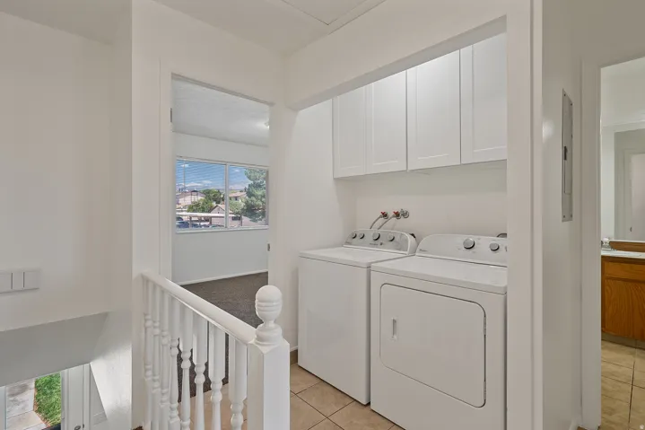 Dedicated laundry area featuring white shaker-style cabinetry, tile flooring, and a balustrade railing