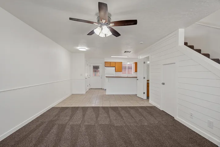 Open-concept living area featuring a ceiling fan with integrated lighting, shiplap accent wall, and wood-finish staircase