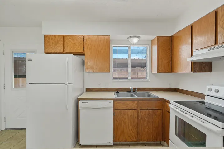 Kitchen featuring wood-finish cabinetry, solid surface countertops, a double basin stainless steel sink, and a white range with overhead vent