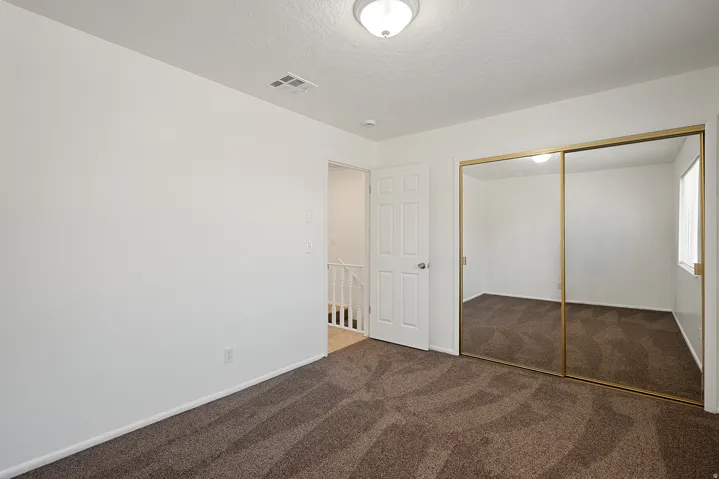 Bedroom featuring neutral wall paint, patterned carpeting, a white paneled door, ceiling-mounted light fixture, and mirrored sliding closet doors