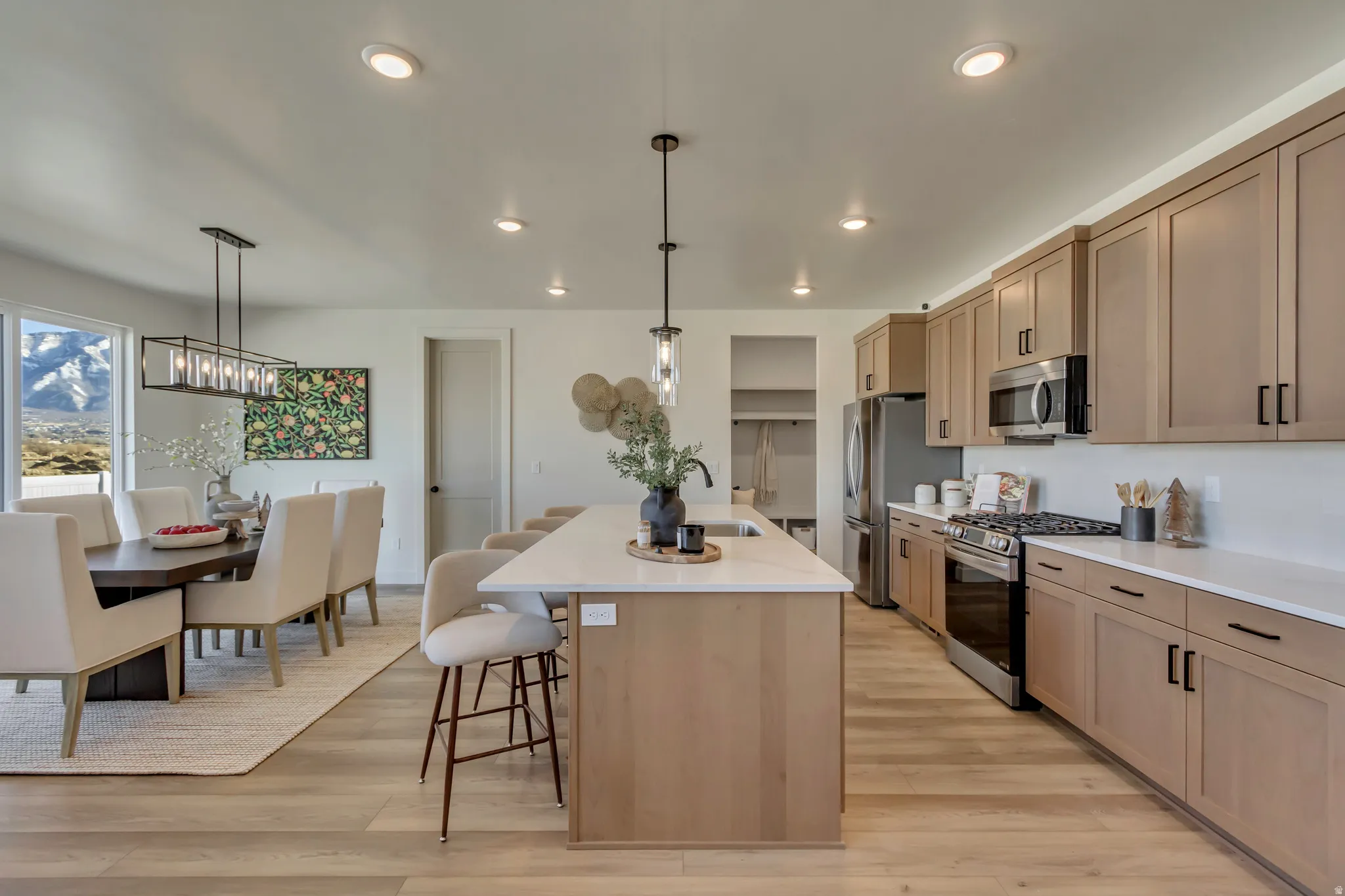 Open-concept kitchen and dining area featuring light wood-finish flooring, recessed lighting, and a linear chandelier