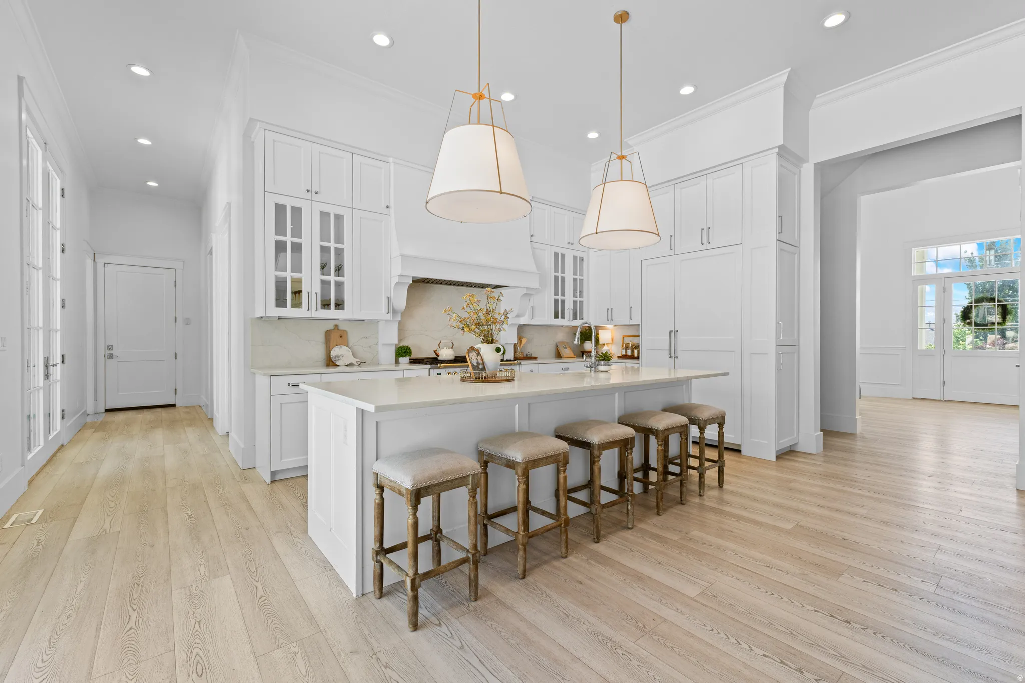 Expansive kitchen featuring white cabinetry, a large center island with seating, pendant lighting, built-in appliances, and light wood-finish flooring
