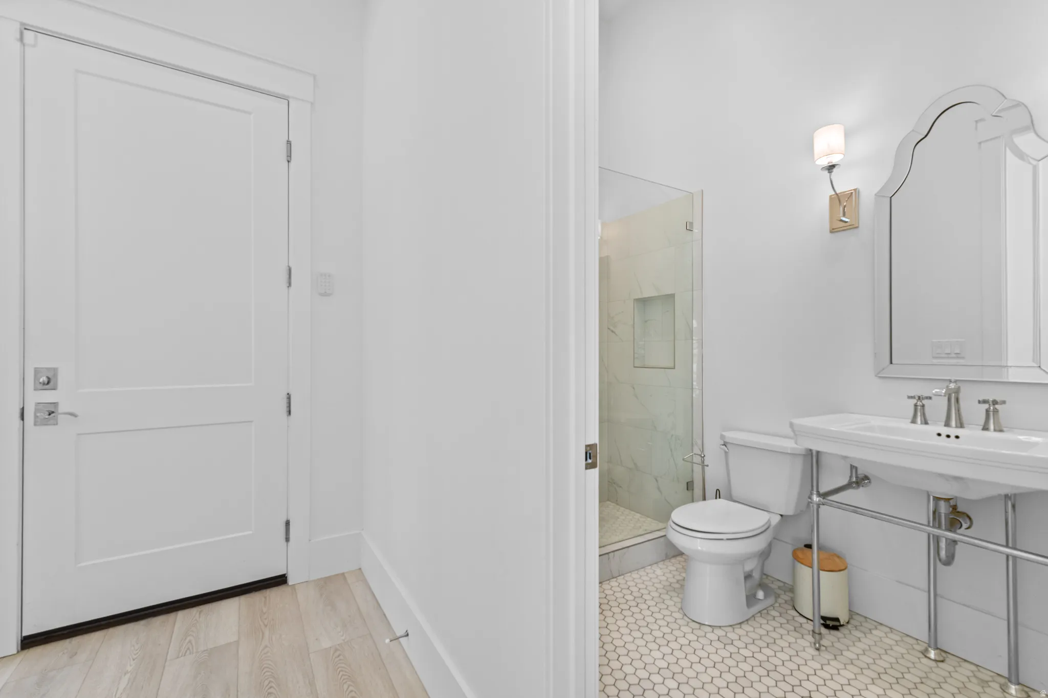 Bathroom featuring a white pedestal sink, frameless glass shower enclosure, white hexagon floor tiling, and a decorative wall mirror