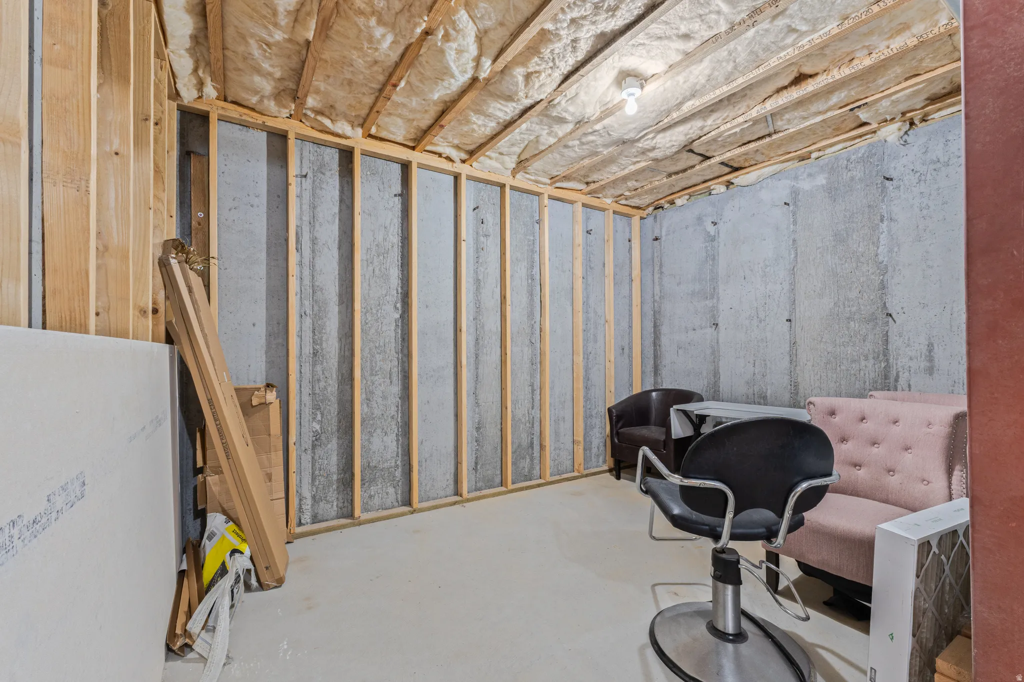 Unfinished basement with concrete walls, exposed wood framing, and ceiling insulation