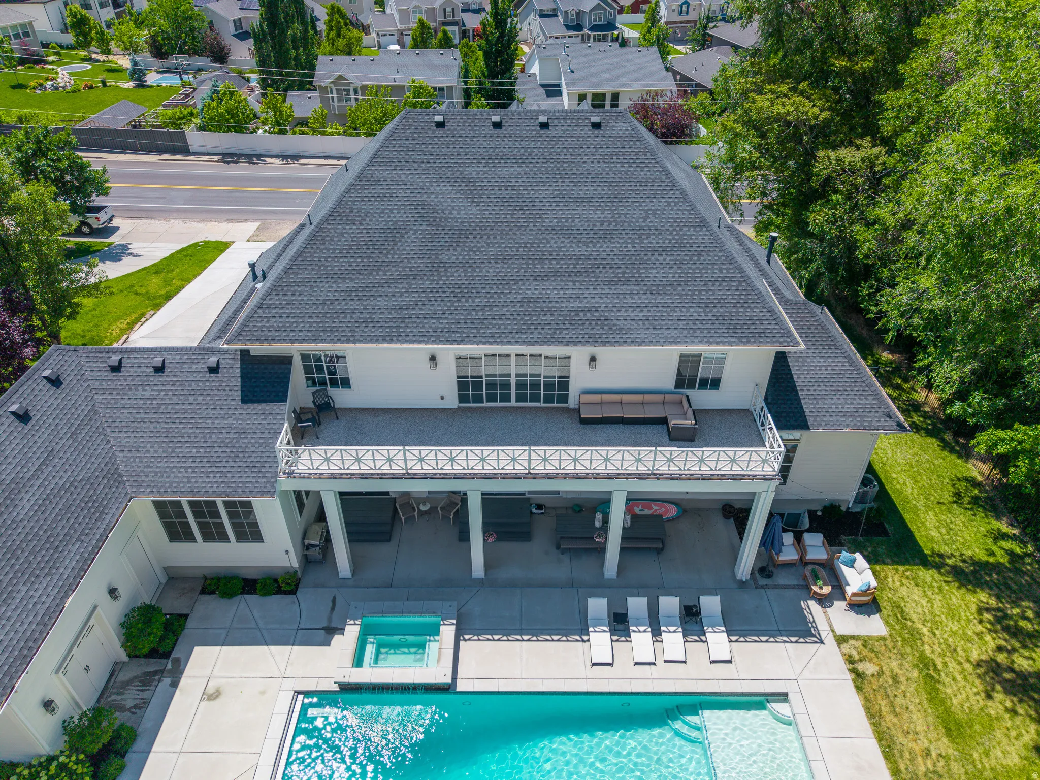 Expansive rear exterior featuring a substantial patio, integrated swimming pool with spa, covered terrace, and a second-story balcony