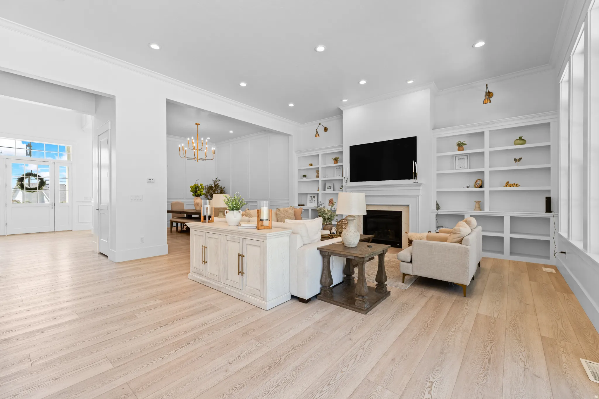Spacious living area featuring light wood-finish flooring, a fireplace with a white mantel, and built-in shelving