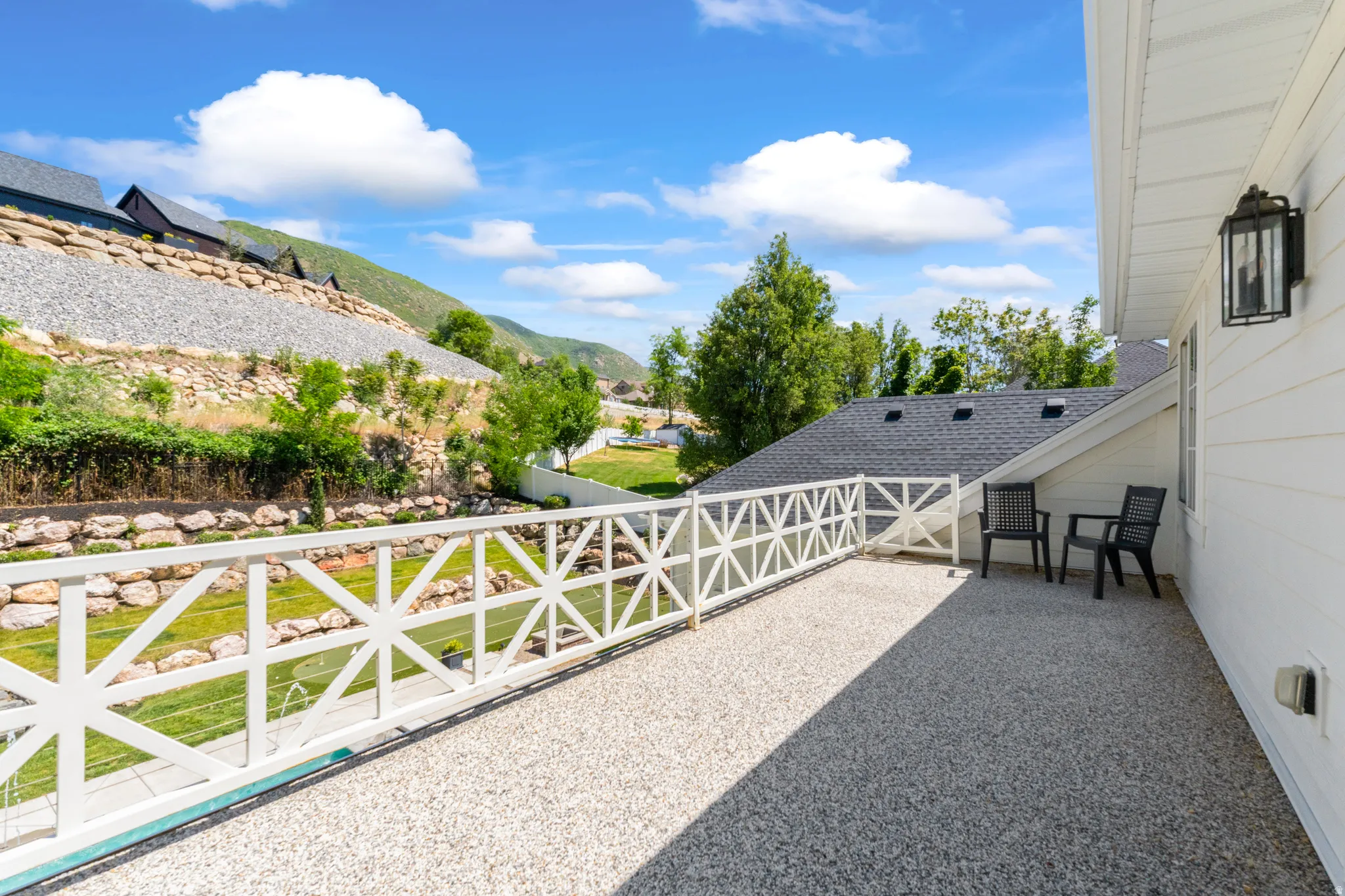 Outdoor terrace featuring a gravel surface, white geometric railing, and exterior wall lighting