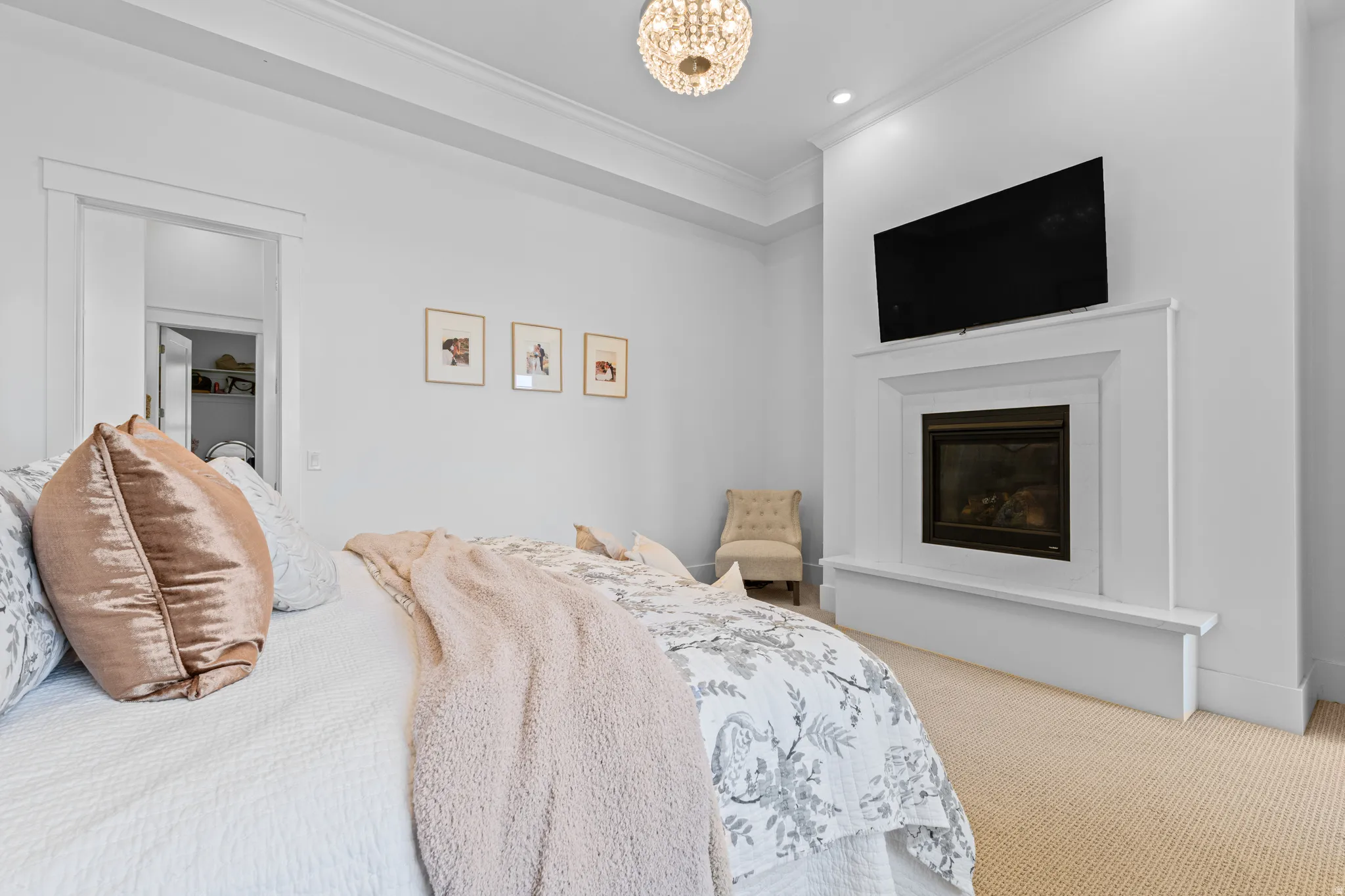 Recessed fireplace with a framed mantel and hearth, tray ceiling with crown molding, and a chandelier-style light fixture