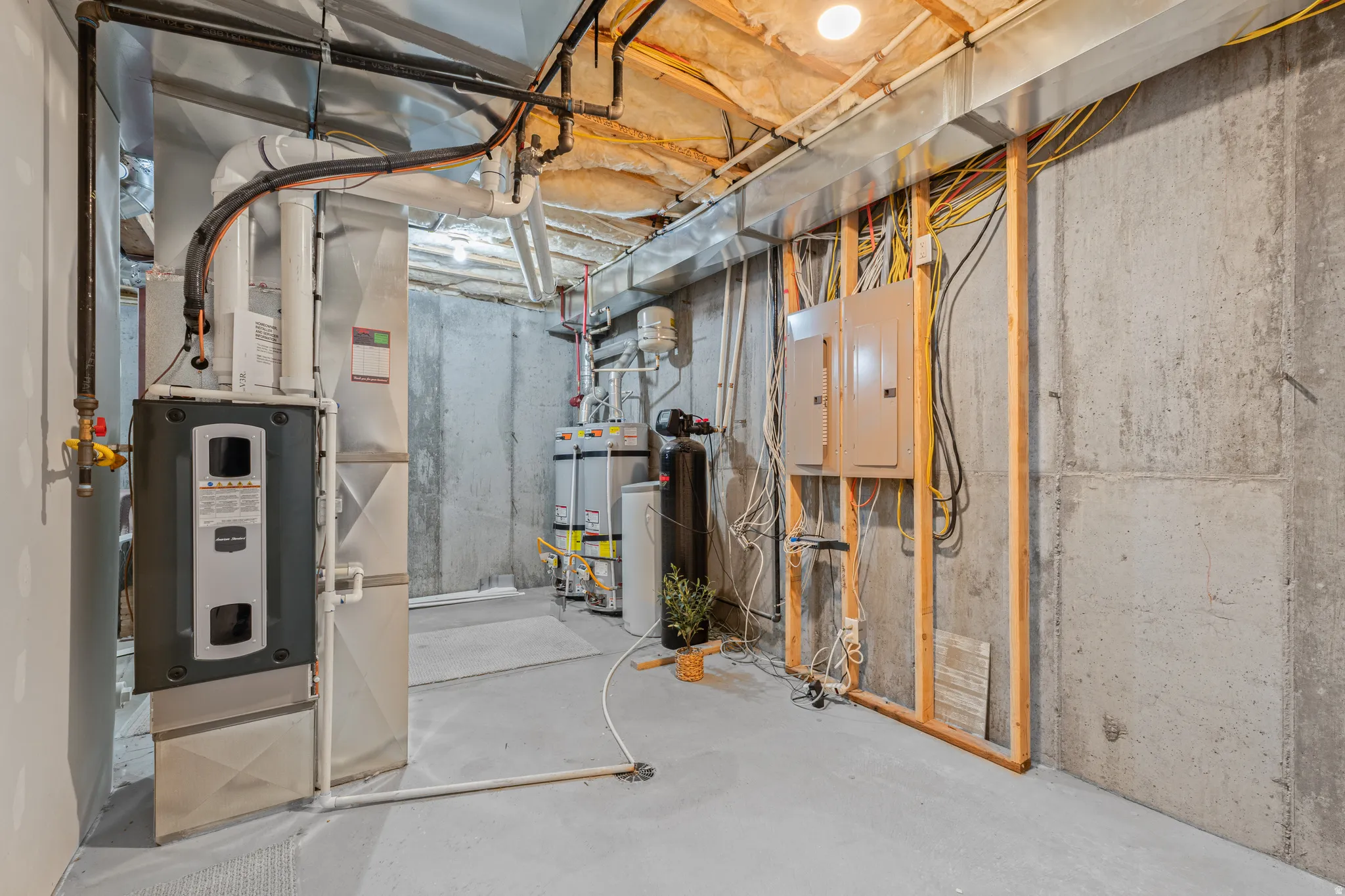 Utility area featuring a furnace system, multiple water heaters, a water filtration system, exposed concrete walls, and electrical panels