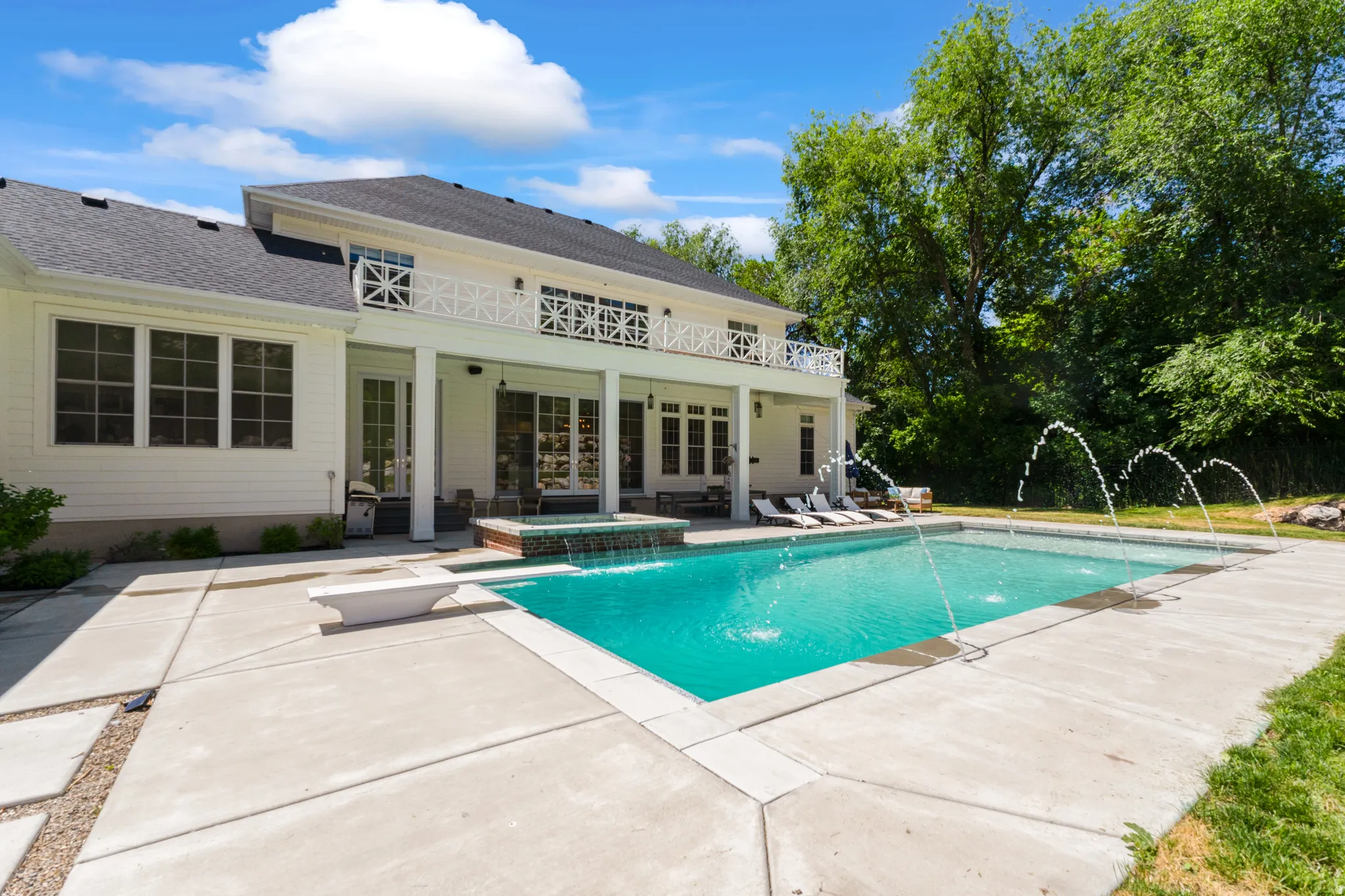 Expansive outdoor living area featuring a large swimming pool with water features, an integrated spa, and a diving board