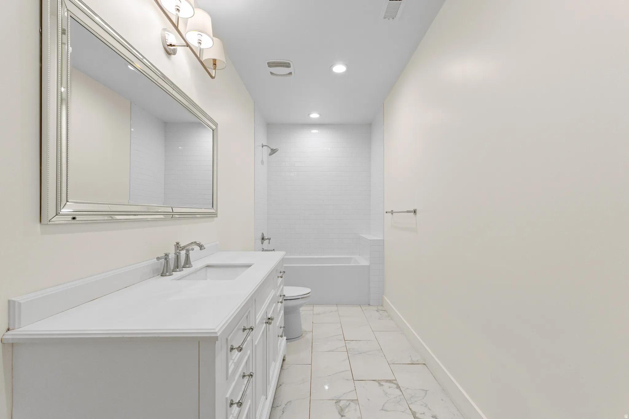White vanity with a single basin, brushed nickel faucet, and a large framed mirror with sconce lighting