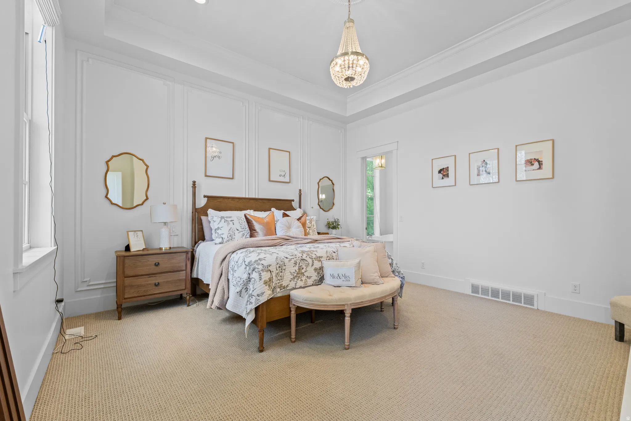 Spacious bedroom featuring tray ceilings, a chandelier, wall paneling, and neutral carpeting