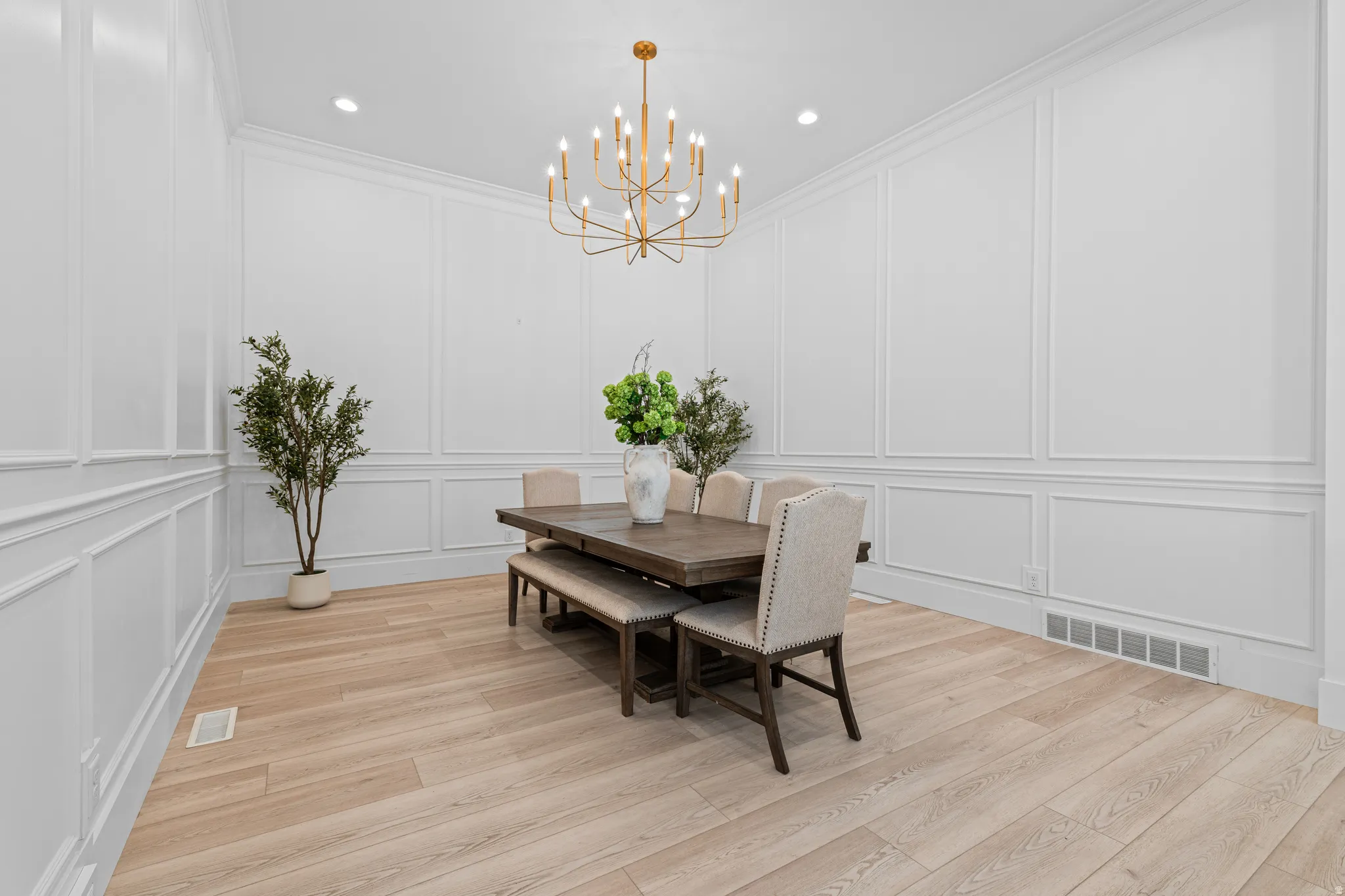 Dining space featuring extensive wall paneling, a contemporary gold-finish chandelier, recessed ceiling lighting, and light wood-finish flooring