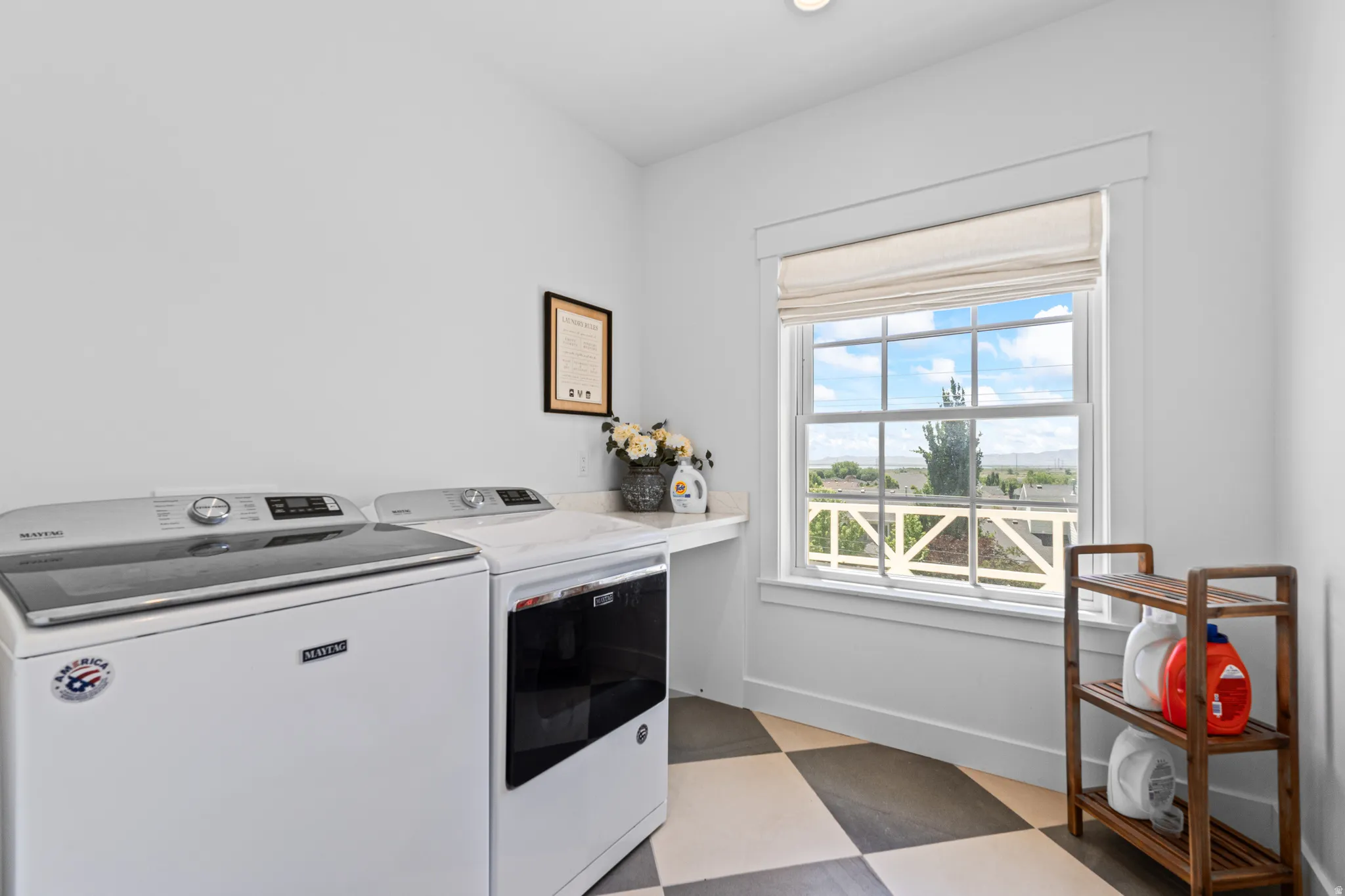 Laundry area featuring a checkered tile floor, a window with a Roman shade, and a built-in countertop