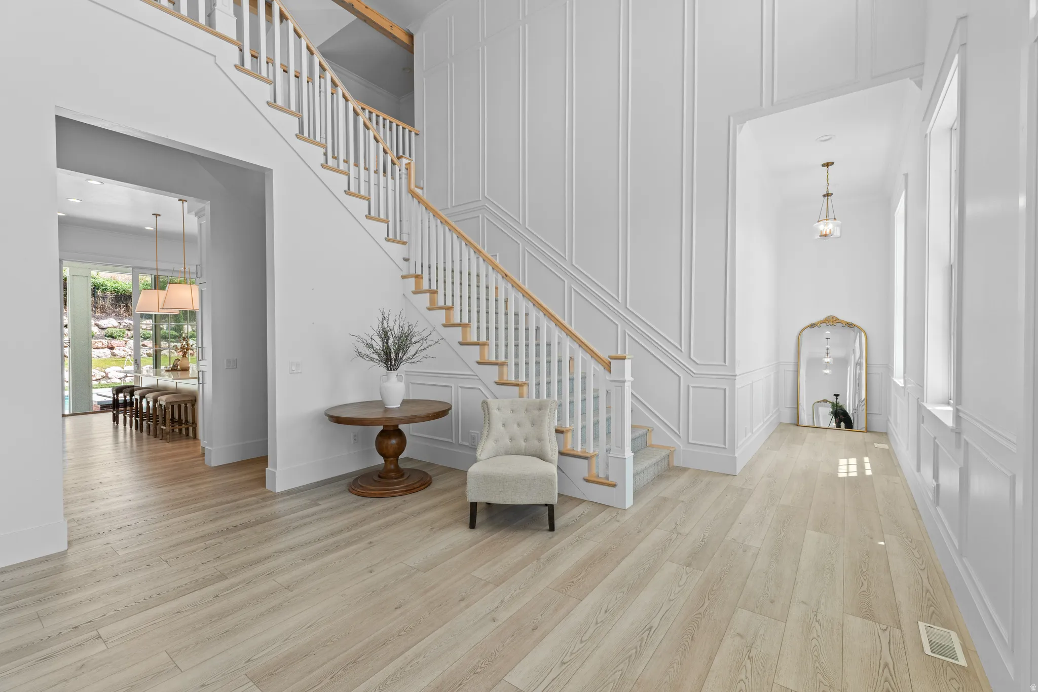 Grand entryway featuring light wood-finish flooring, a prominent staircase with white balusters and natural wood handrails, and extensive white wall paneling