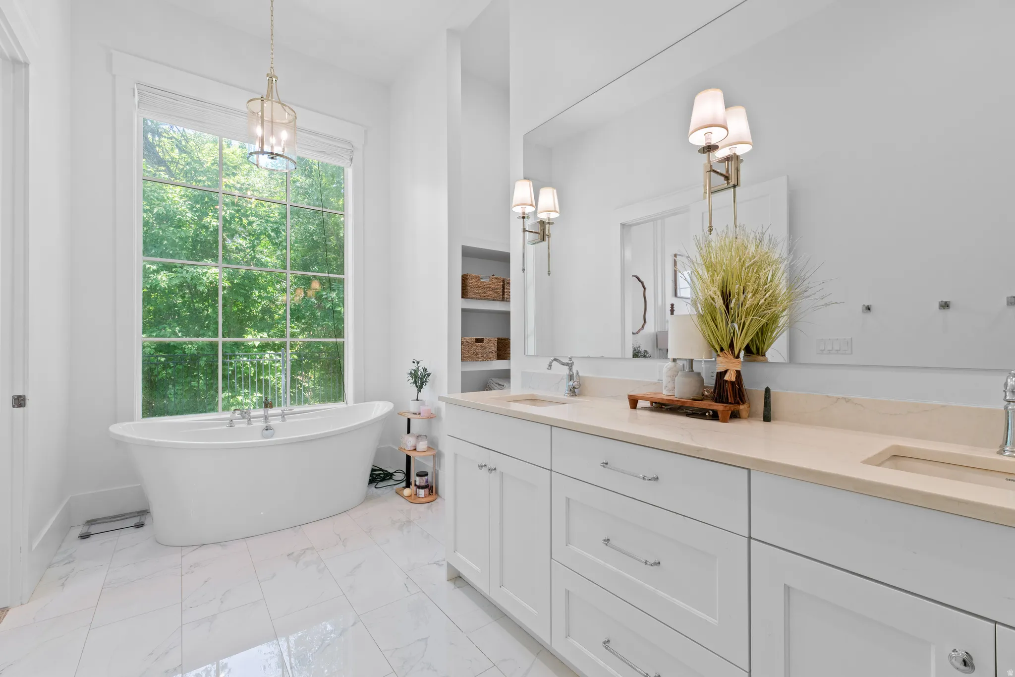 Freestanding soaking tub beneath a large window, complemented by a dual vanity with light-toned countertops, white cabinetry, and wall-mounted sconces