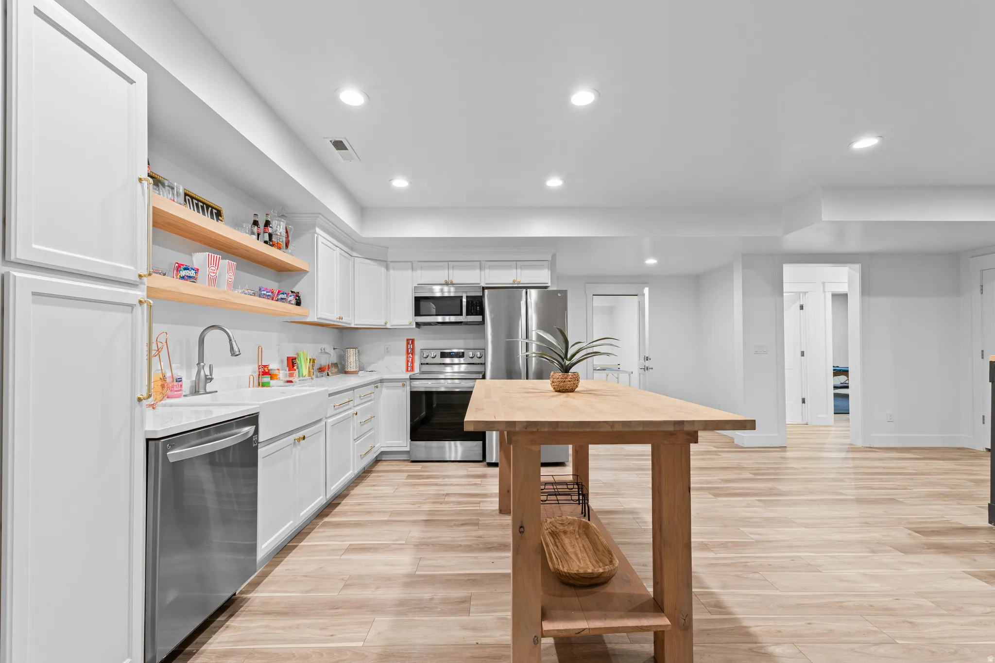 Modern kitchen featuring white cabinetry, stainless steel appliances, a farmhouse sink, open wood shelving, and light wood-finish flooring
