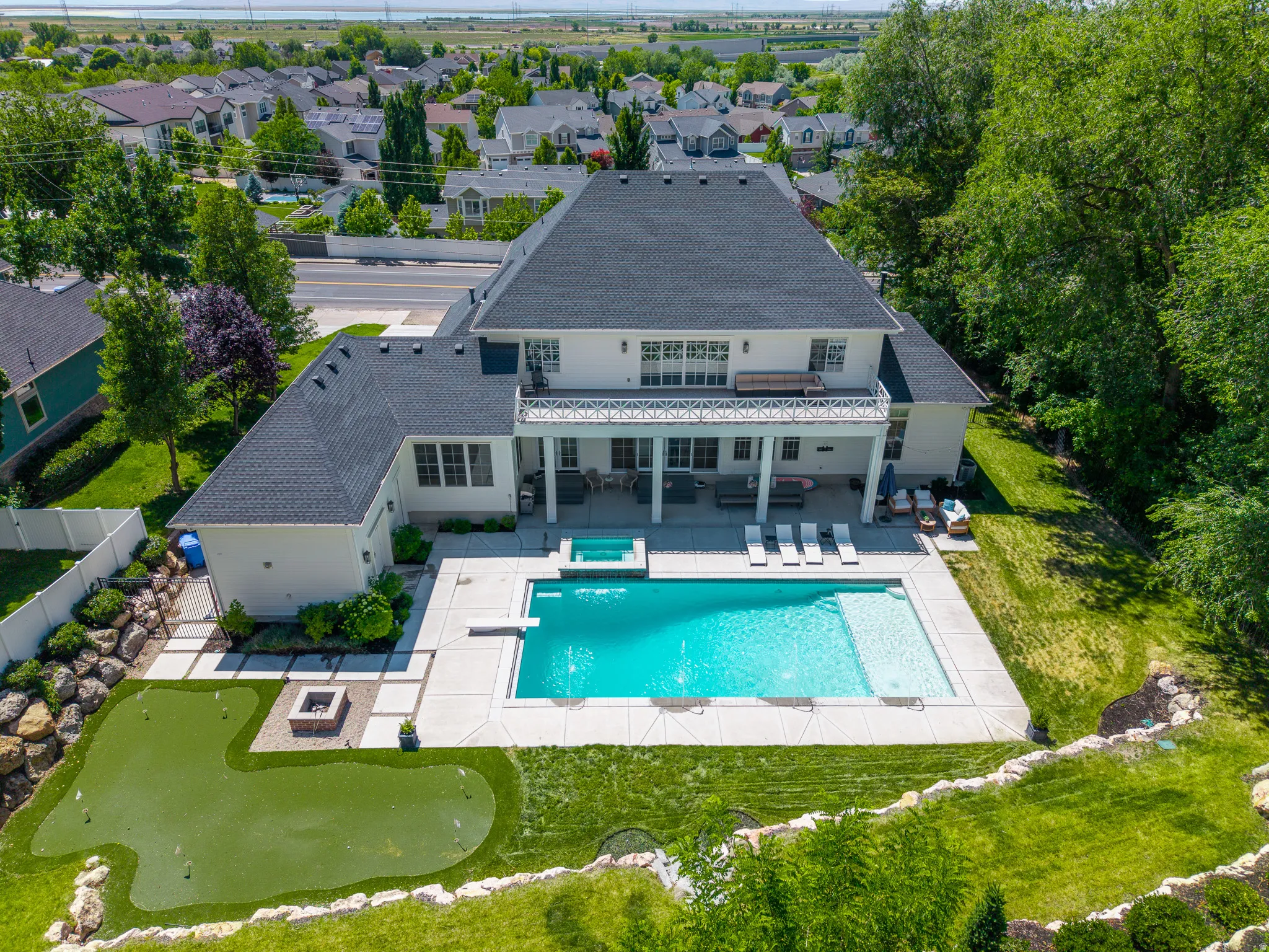 Expansive rear exterior featuring a large swimming pool with integrated spa, a dedicated putting green, and a fire pit area