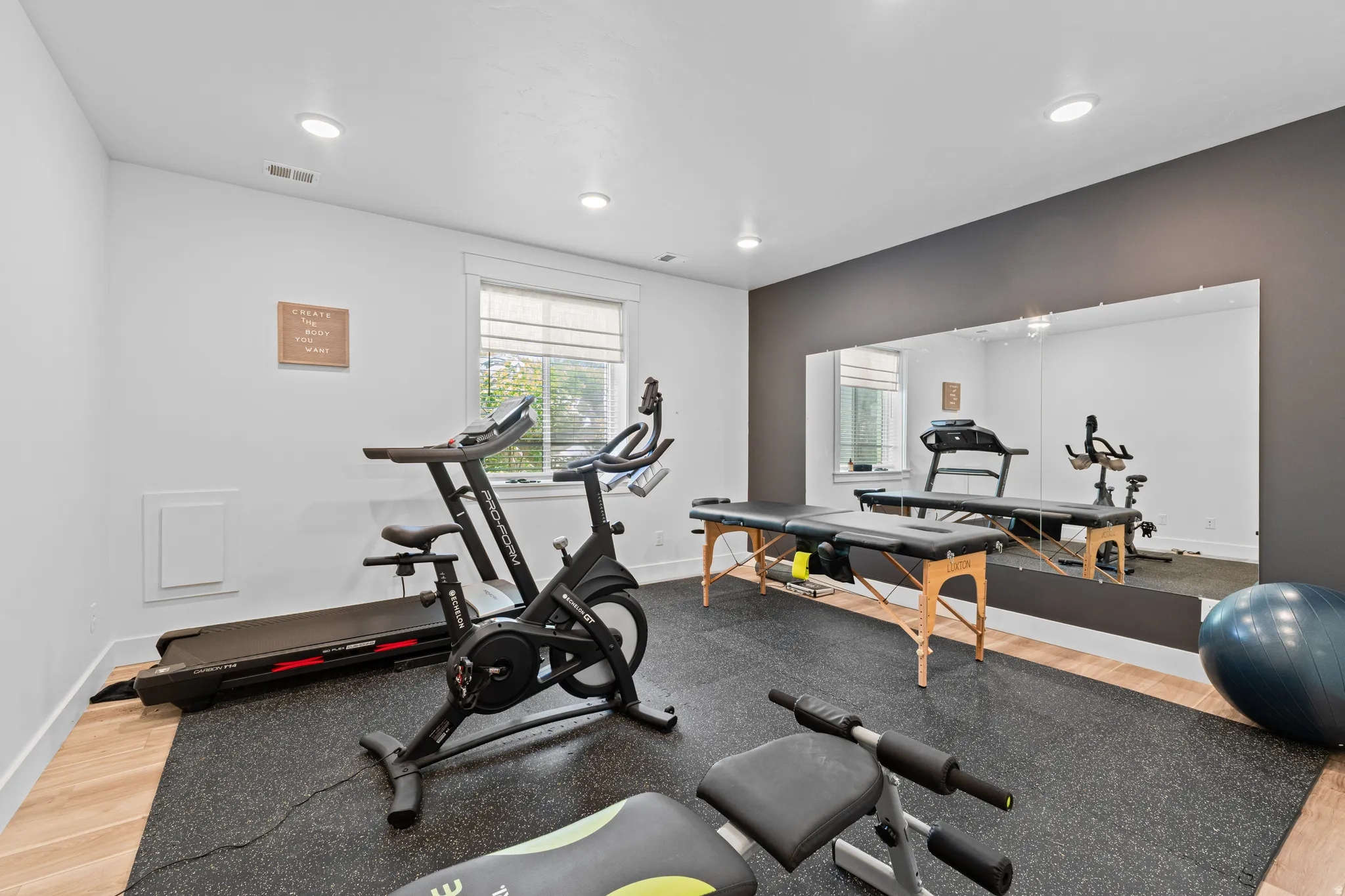 Dedicated fitness space featuring rubber flooring, a full-wall mirror, recessed lighting, a window with blinds, and contrasting accent wall