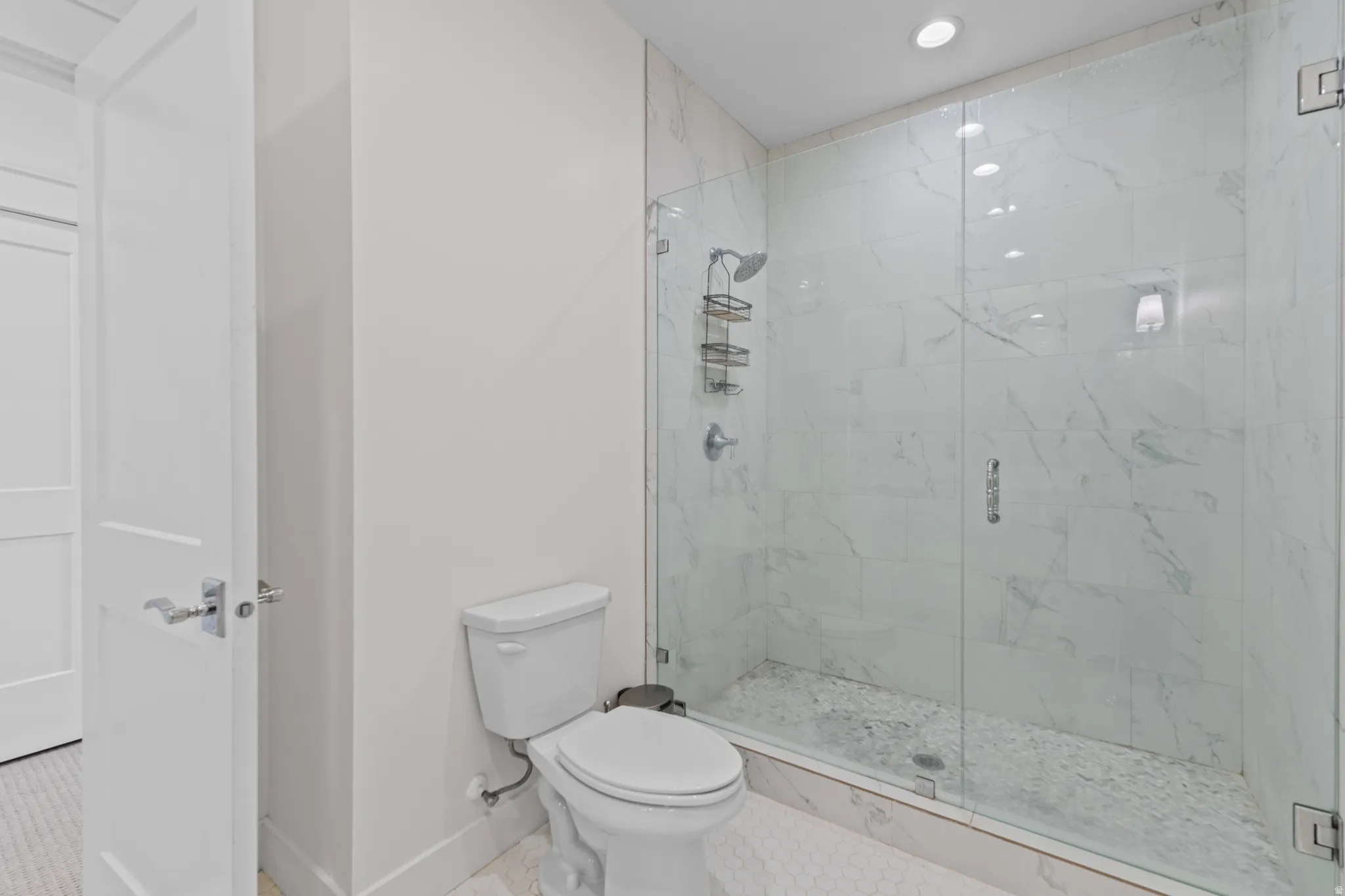 Walk-in shower with clear glass enclosure, white marbled tile surround, and pebble stone floor